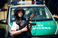Uczennica klasy policyjnej przebrana w kask, kamizelkę kuloodporną z karabinem w ręce na tle pojazdu Straży Granicznej