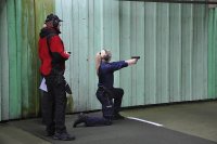 policjantka strzela w pozycji klęczącej, instruktor obserwuje z tyłu